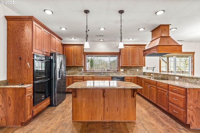 kitchen featuring a center island, decorative light fixtures, a sink, light stone countertops, and black appliances