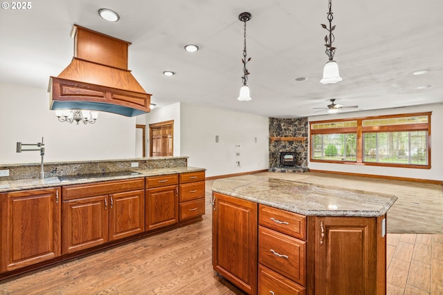 kitchen with a kitchen island, brown cabinets, light stone countertops, light wood-style floors, and pendant lighting