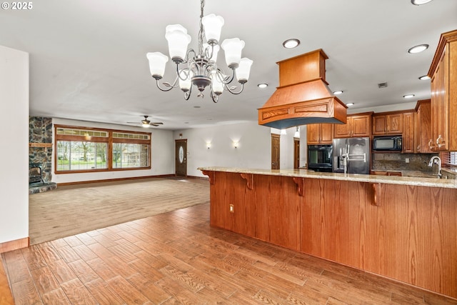 kitchen featuring light wood finished floors, a breakfast bar, a peninsula, black microwave, and stainless steel refrigerator with ice dispenser