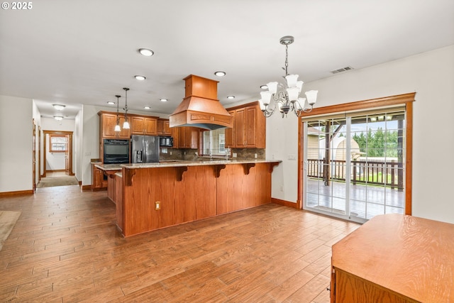 kitchen featuring decorative light fixtures, visible vents, custom range hood, a peninsula, and black appliances