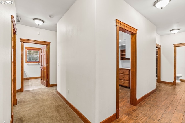 hallway with light wood-type flooring, visible vents, and baseboards