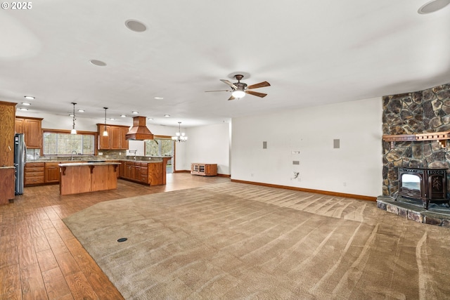 living area with baseboards, a wood stove, ceiling fan with notable chandelier, light wood-type flooring, and recessed lighting