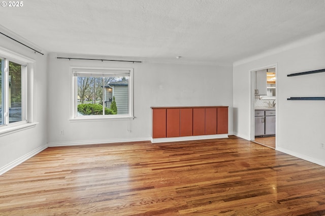 unfurnished room featuring light wood finished floors, a textured ceiling, and baseboards