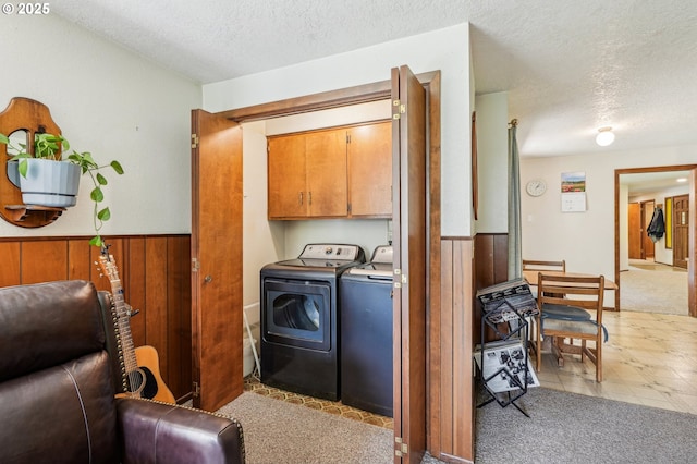 washroom with wainscoting, a textured ceiling, washing machine and dryer, and cabinet space