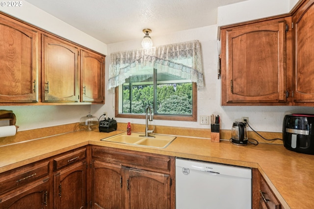 kitchen with brown cabinetry, a sink, dishwasher, and light countertops