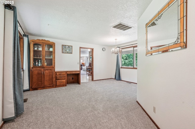 carpeted empty room with a textured ceiling, a notable chandelier, visible vents, and baseboards