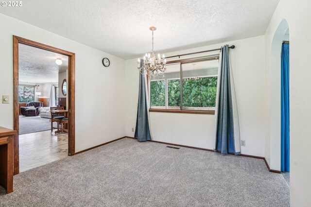 carpeted spare room with an inviting chandelier, arched walkways, a textured ceiling, and baseboards