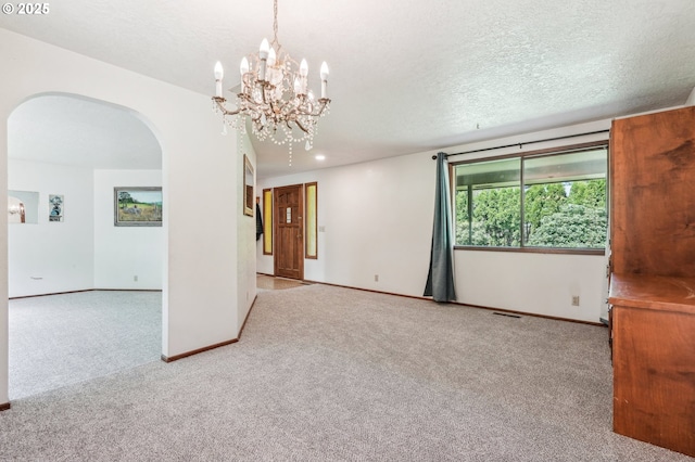 carpeted spare room with arched walkways, baseboards, visible vents, and an inviting chandelier