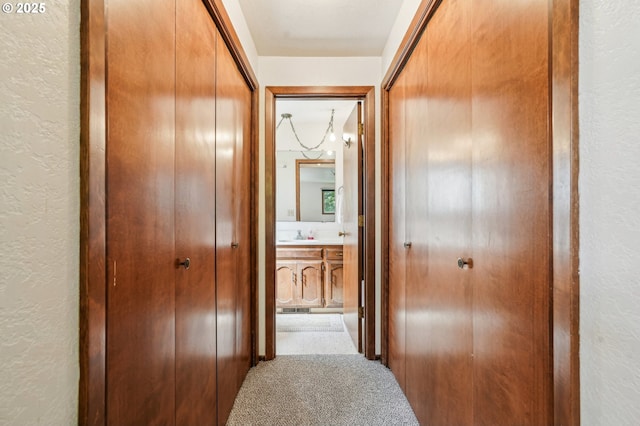 corridor with a textured wall, visible vents, a sink, and carpet