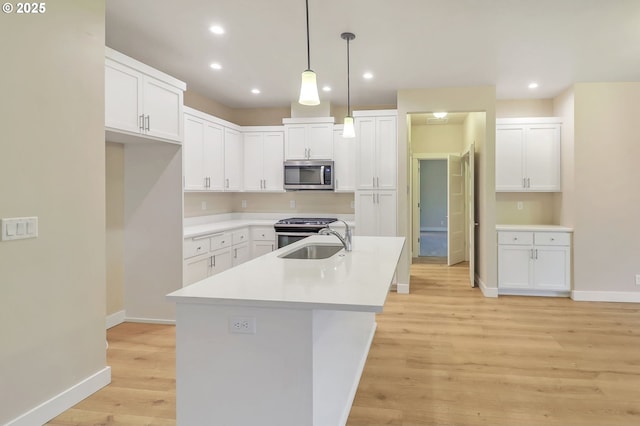 kitchen featuring decorative light fixtures, stainless steel appliances, a kitchen island with sink, white cabinetry, and sink