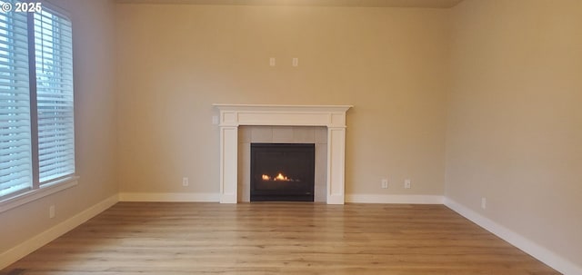 unfurnished living room with light wood-type flooring and a tiled fireplace