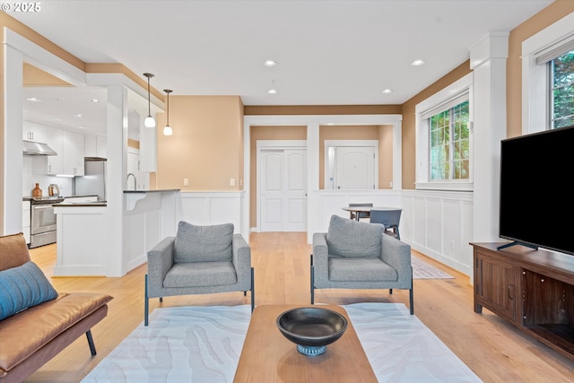 living room featuring wainscoting, a decorative wall, light wood-type flooring, and recessed lighting
