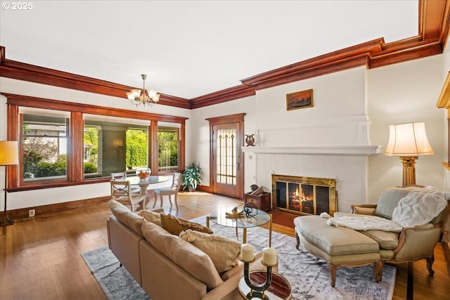 living room with crown molding, hardwood / wood-style flooring, baseboards, a notable chandelier, and a glass covered fireplace