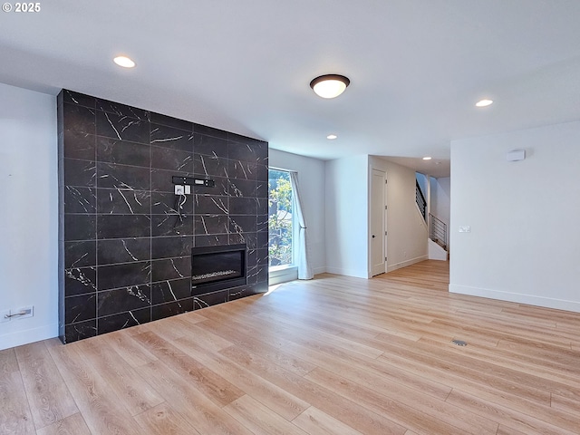 unfurnished living room featuring wood finished floors, recessed lighting, a high end fireplace, baseboards, and stairway