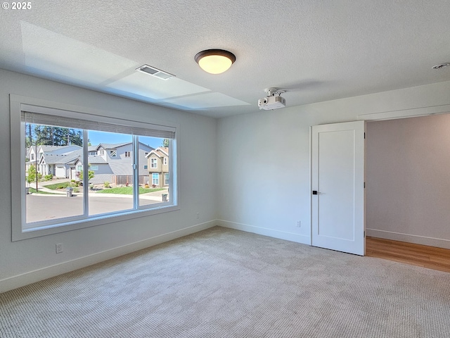 empty room with baseboards, a textured ceiling, and light carpet