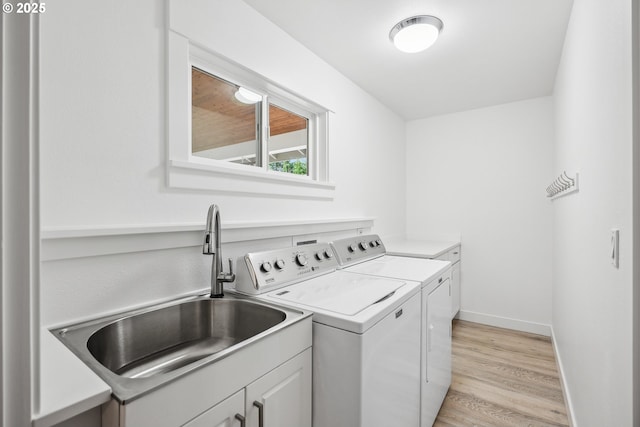 clothes washing area featuring light wood finished floors, baseboards, separate washer and dryer, cabinet space, and a sink