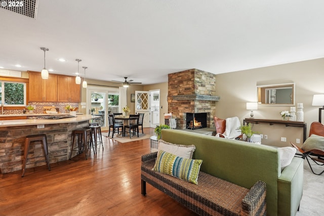 living room featuring wood finished floors, visible vents, recessed lighting, ceiling fan, and a stone fireplace