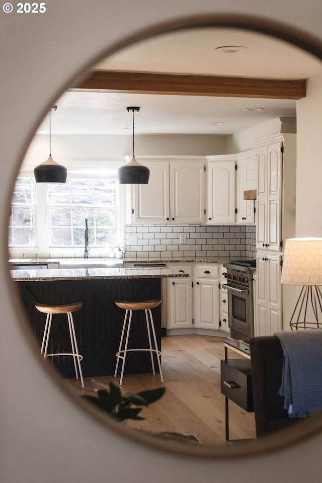 kitchen with a sink, light wood finished floors, white cabinets, high end stainless steel range oven, and beam ceiling