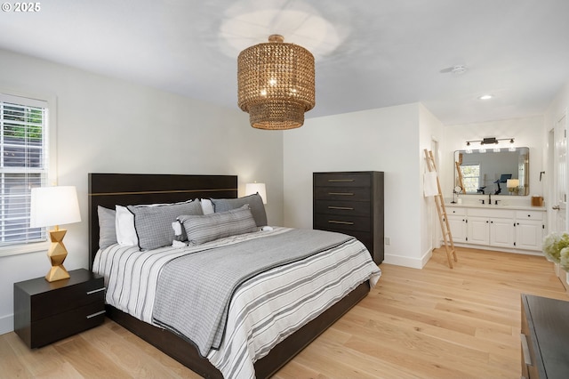 bedroom featuring light wood finished floors, ensuite bathroom, baseboards, recessed lighting, and a notable chandelier
