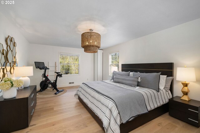bedroom featuring light wood-style floors, multiple windows, and an inviting chandelier