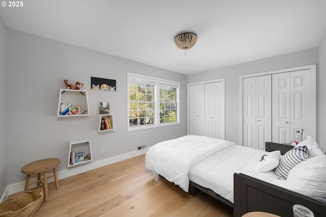 bedroom featuring light wood-type flooring, baseboards, visible vents, and two closets