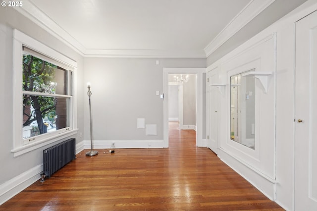spare room featuring ornamental molding, radiator, wood finished floors, and a notable chandelier