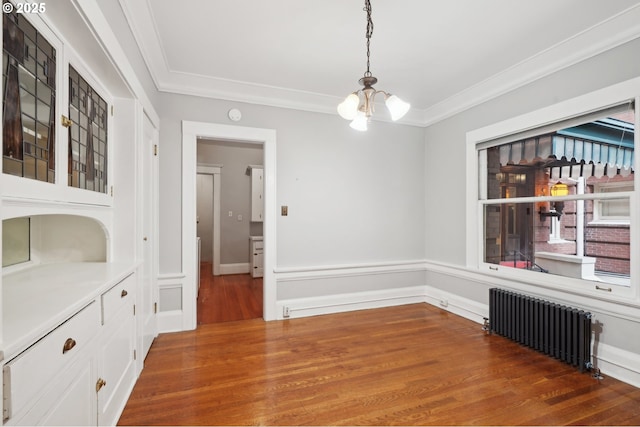 unfurnished dining area with a chandelier, radiator heating unit, baseboards, wood finished floors, and ornamental molding