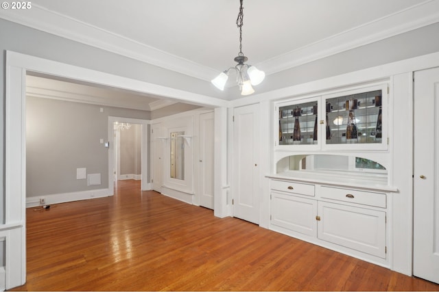 unfurnished dining area with baseboards, a notable chandelier, ornamental molding, and light wood-style flooring