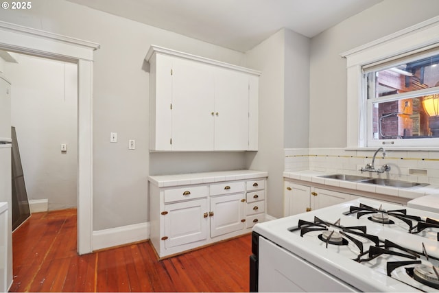 kitchen with white gas range oven, wood finished floors, tile countertops, white cabinetry, and a sink
