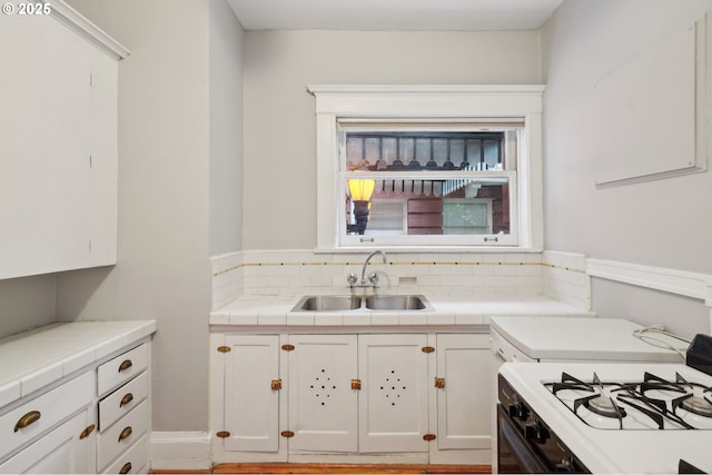 kitchen featuring white cabinets, gas range gas stove, a sink, and tasteful backsplash