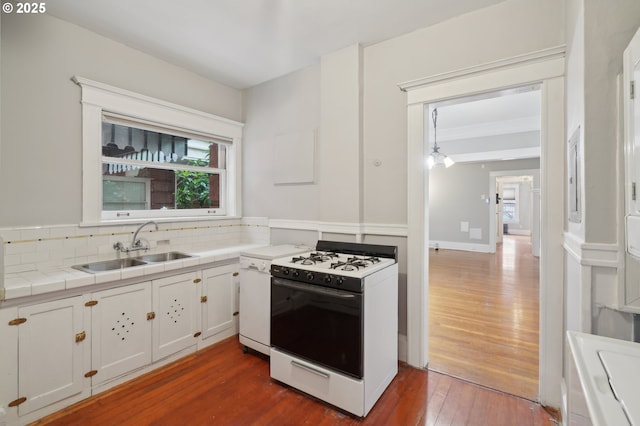 kitchen with dark wood-style flooring, a sink, tile counters, gas range gas stove, and tasteful backsplash