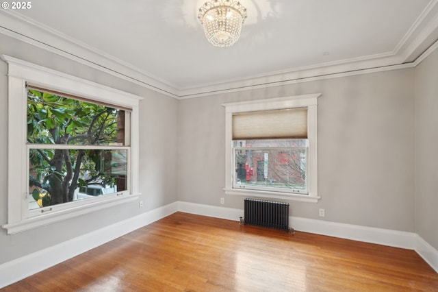 empty room with radiator, ornamental molding, wood finished floors, and a notable chandelier