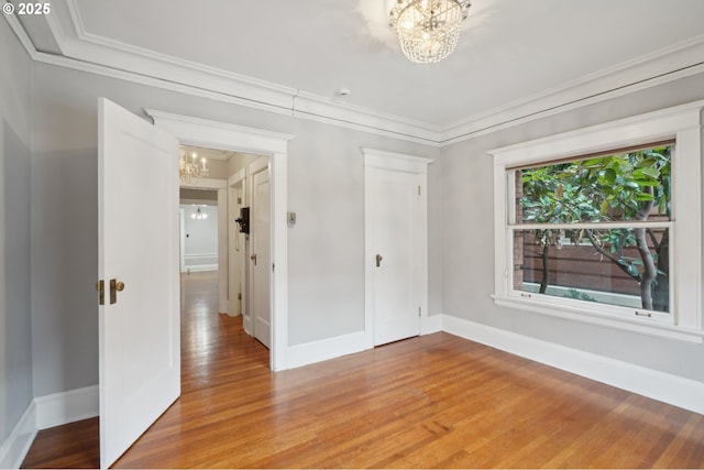 spare room with crown molding, baseboards, a notable chandelier, and wood finished floors