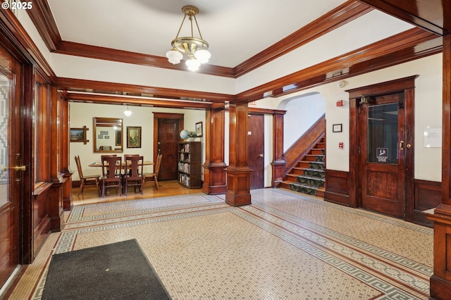entryway featuring crown molding, a notable chandelier, stairs, and a wainscoted wall