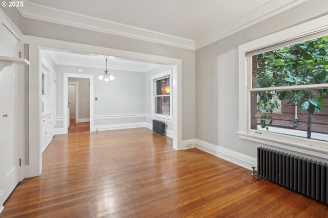 unfurnished room with wood finished floors, baseboards, a chandelier, radiator, and ornamental molding