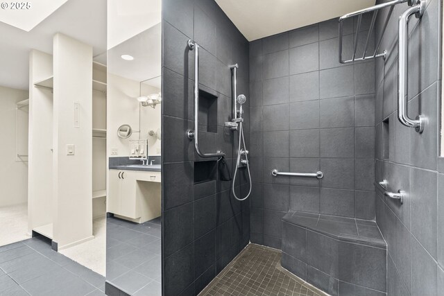 bathroom featuring tile patterned flooring, a walk in closet, a tile shower, and vanity
