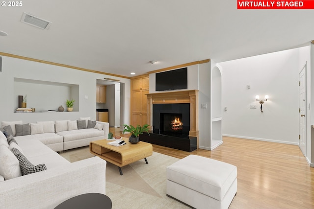 living room featuring visible vents, light wood-style floors, baseboards, and a warm lit fireplace