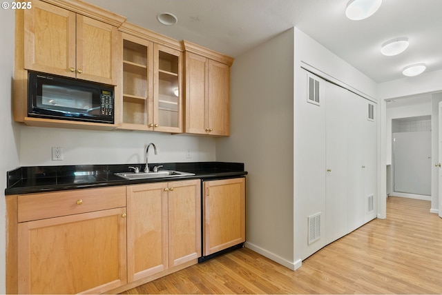 kitchen with black microwave, dark countertops, baseboards, a sink, and light wood finished floors