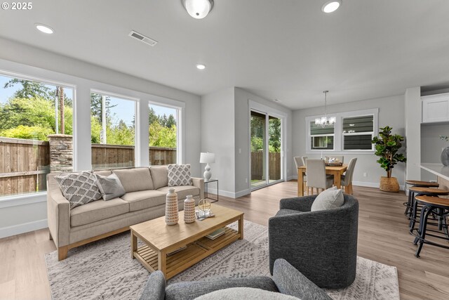 living area with visible vents, baseboards, light wood finished floors, a notable chandelier, and recessed lighting