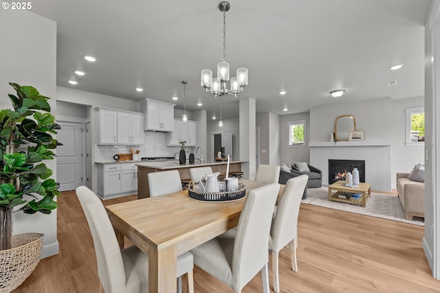 dining area featuring light wood-style flooring, a chandelier, a wealth of natural light, and a fireplace