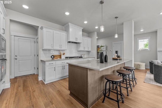 kitchen featuring light countertops, a breakfast bar area, white cabinetry, decorative backsplash, and light wood-type flooring