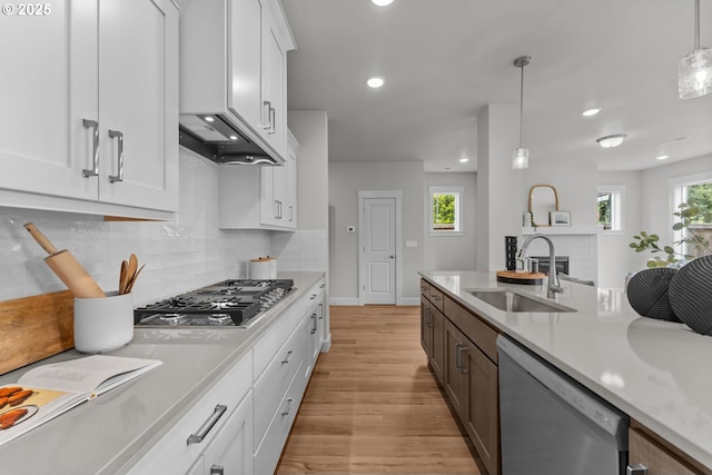 kitchen featuring appliances with stainless steel finishes, hanging light fixtures, light countertops, a sink, and light wood-style flooring