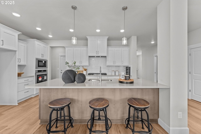 kitchen featuring backsplash, appliances with stainless steel finishes, a sink, white cabinets, and light wood finished floors