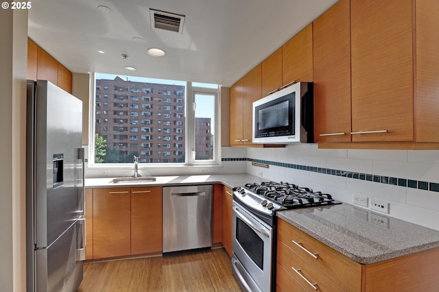 kitchen with tasteful backsplash, light hardwood / wood-style floors, sink, appliances with stainless steel finishes, and light stone counters