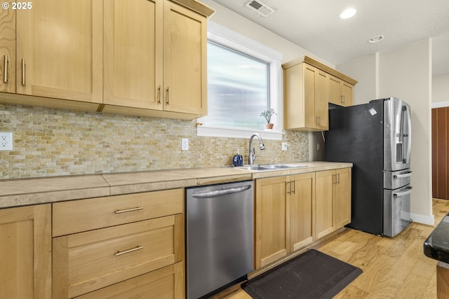 kitchen with a sink, light brown cabinetry, stainless steel appliances, and light wood finished floors