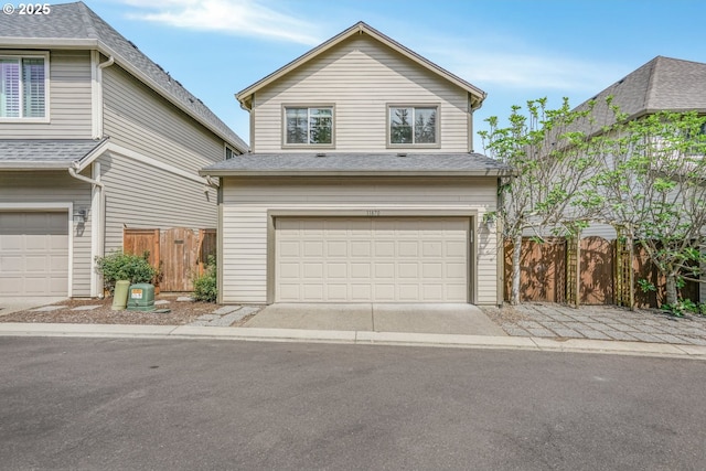 traditional home featuring an attached garage, a shingled roof, fence, and driveway