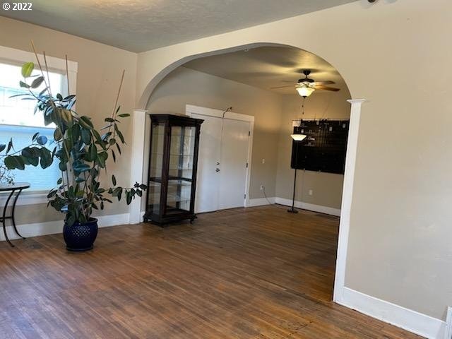 interior space with baseboards, ceiling fan, arched walkways, and wood finished floors