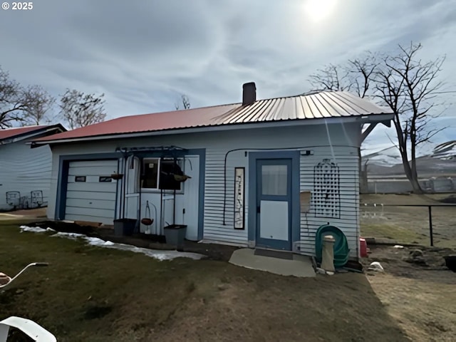 rear view of property featuring metal roof, a garage, and a chimney