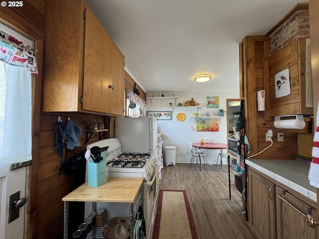 kitchen with brown cabinets, light countertops, dark wood-type flooring, and white gas range oven