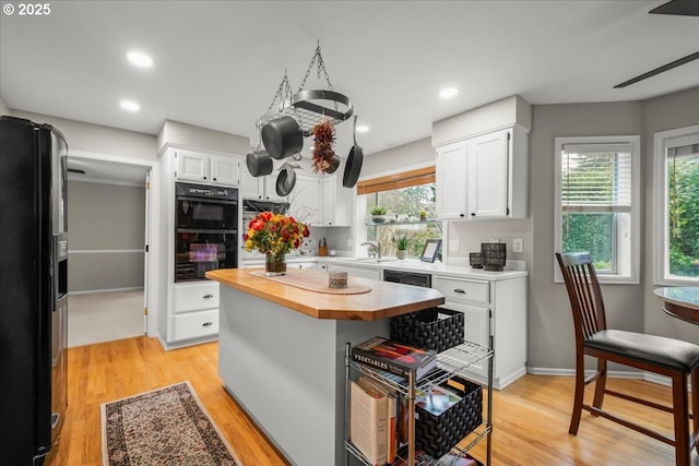 kitchen with white cabinets, wood counters, black appliances, and light wood finished floors